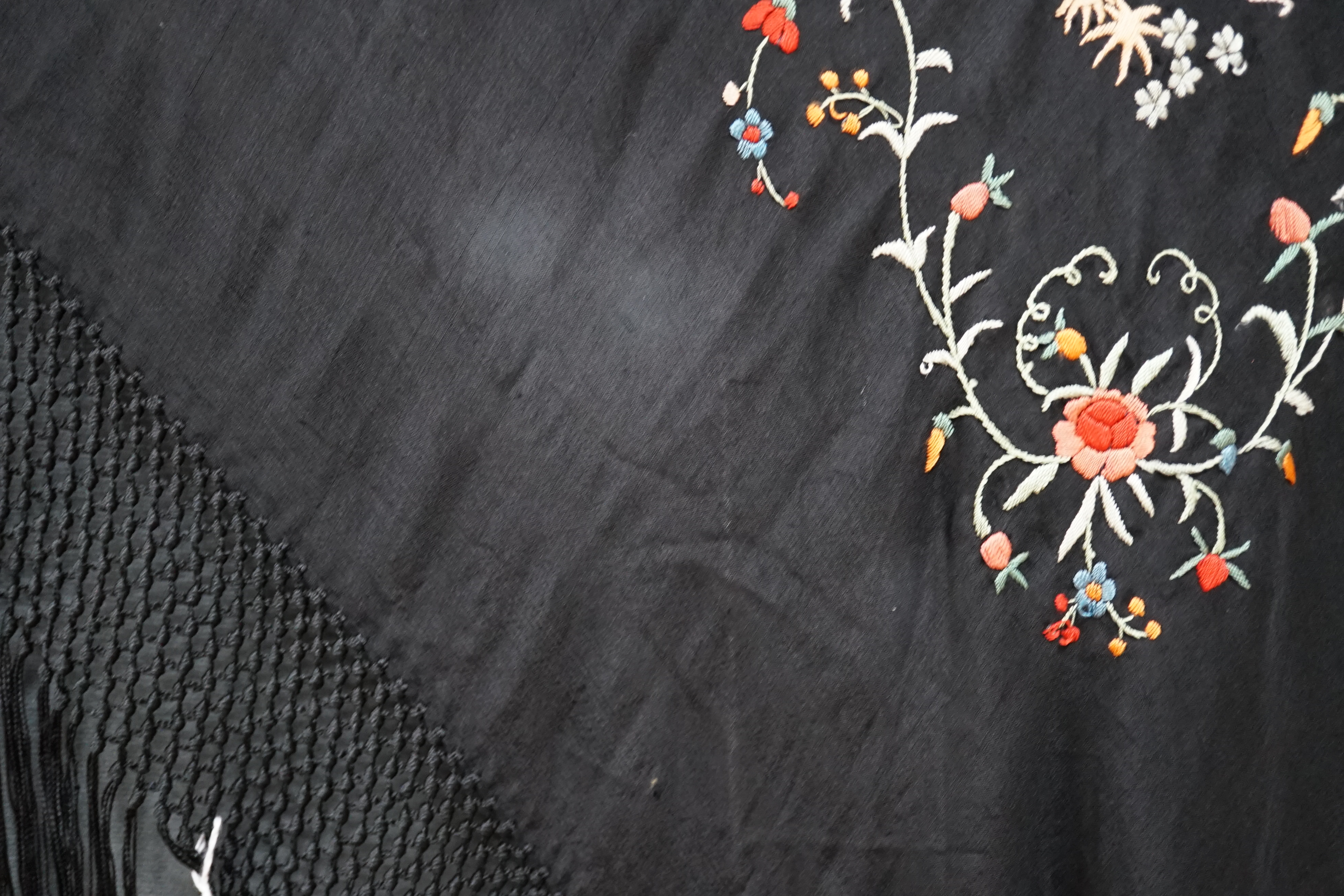 An early 20th century Chinese black silk shawl, with all over coloured floral embroidery, embroidered with multi-coloured silks and a long silk fringe, unusually the four corners are embroidered with a figurative pagoda